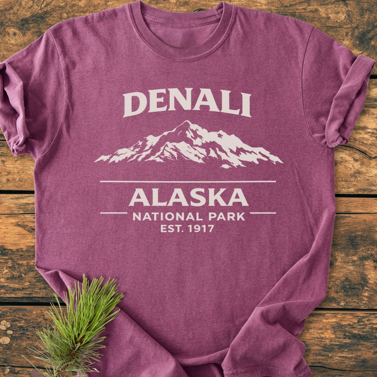 Denali Alaska National Park - Vintage Wash Tee in heathered-purple featuring a mountain graphic and text design; displayed on wood with an evergreen sprig, showcasing its relaxed fit and durability.
