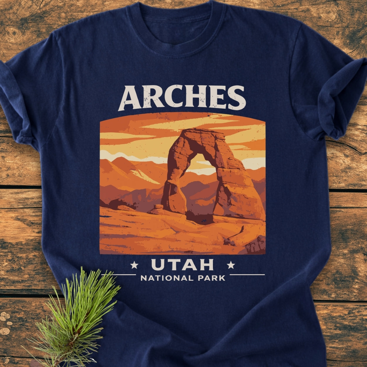 Arches Utah National Park - Vintage Wash Tee displayed on wood, featuring a stylized print of Delicate Arch. A pine sprig complements this Comfort Colors garment-dyed tee, enhancing its cozy, relaxed appeal.