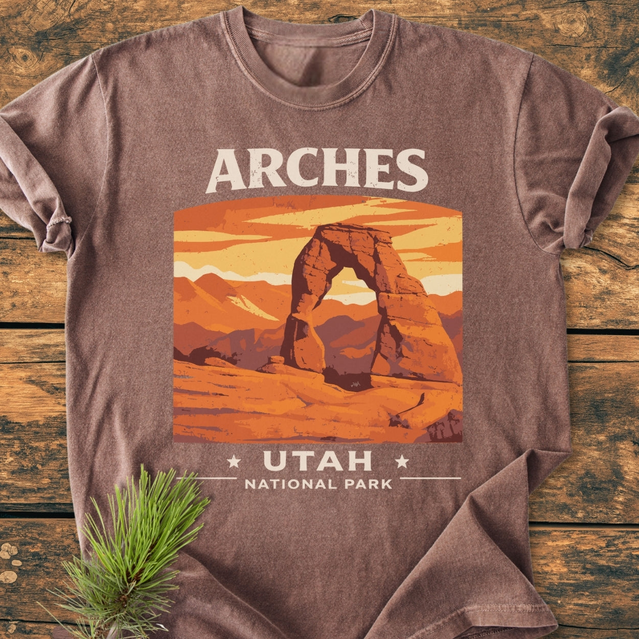 Arches Utah National Park - Vintage Wash Tee featuring a sandstone arch design on a laid-flat, earth-toned shirt with pine sprig beside it, highlighting its cozy, relaxed fit and durable construction.