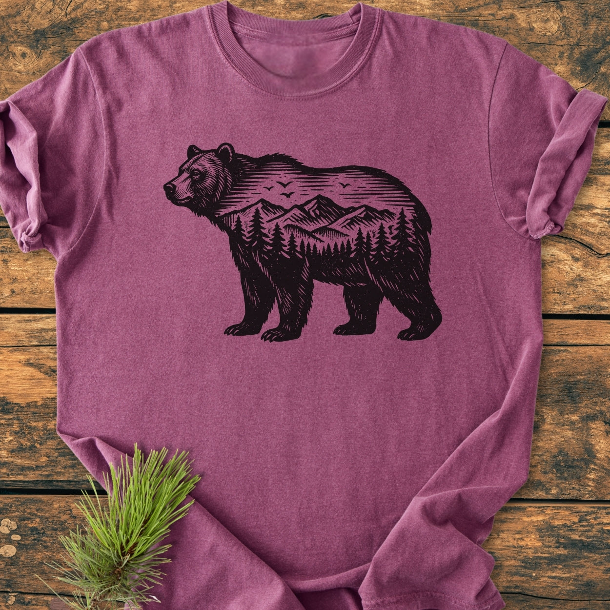 The Wilderness Within - Vintage Wash Tee showcases a bear silhouette with a mountain scene, printed on a heather-purple shirt, laid on a wooden surface, emphasizing its soft, relaxed fit.