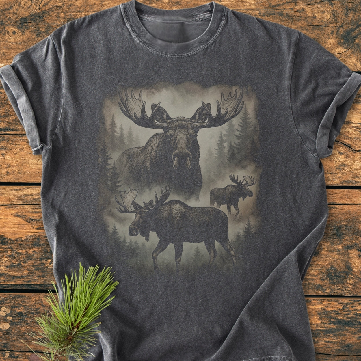 Shadow Moose - Vintage Wash Tee on wooden surface, featuring moose silhouettes with misty evergreens. Comfortable, relaxed fit, garment-dyed 100% ring-spun cotton, ideal for daily wear.
