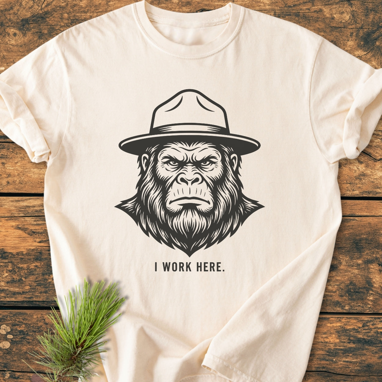 I Work Here - Vintage Wash Tee features a stern gorilla in a ranger hat with text beneath. Laid flat on wood, highlighting its relaxed fit and durable stitching.