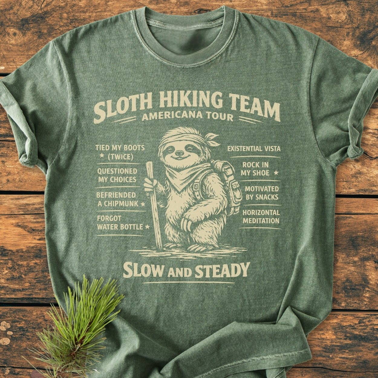 Sloth Hiking Team Tour - Vintage Wash Tee features a smiling sloth with hiking gear and humorous trail achievements, printed on a soft, relaxed-fit, heather-green T-shirt, ideal for casual wear.