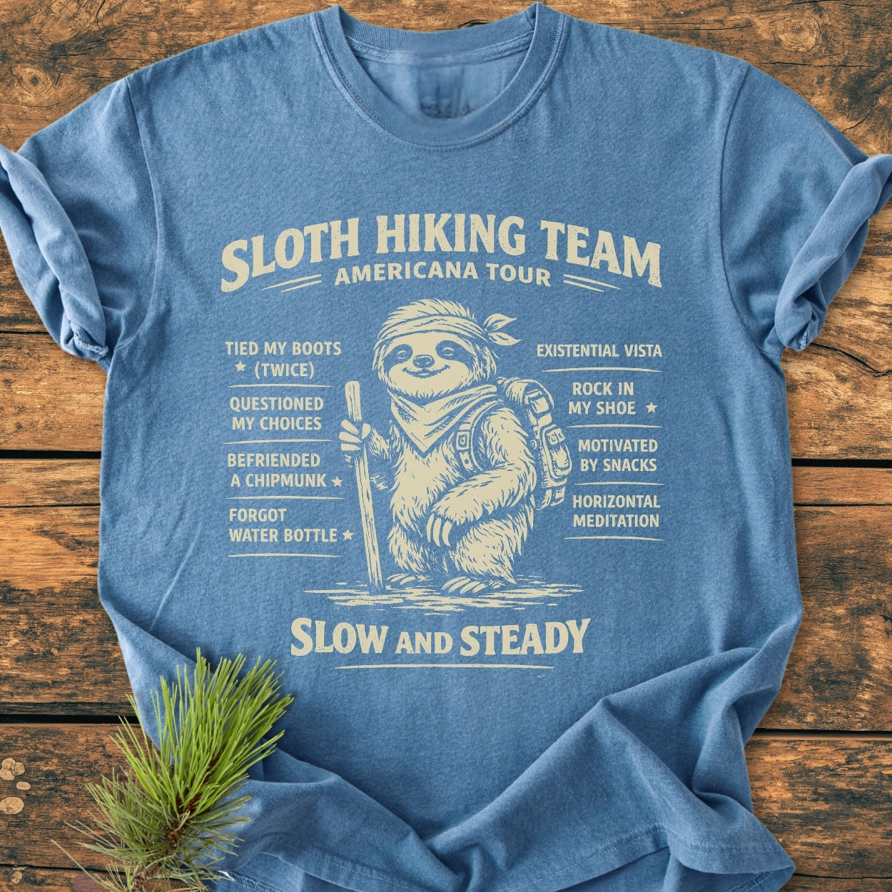 Sloth Hiking Team Tour - Vintage Wash Tee displays a sloth graphic with hiking gear and humorous achievements, highlighting its cozy, relaxed fit and durable, pre-shrunk cotton fabric on a heather-blue T-shirt.