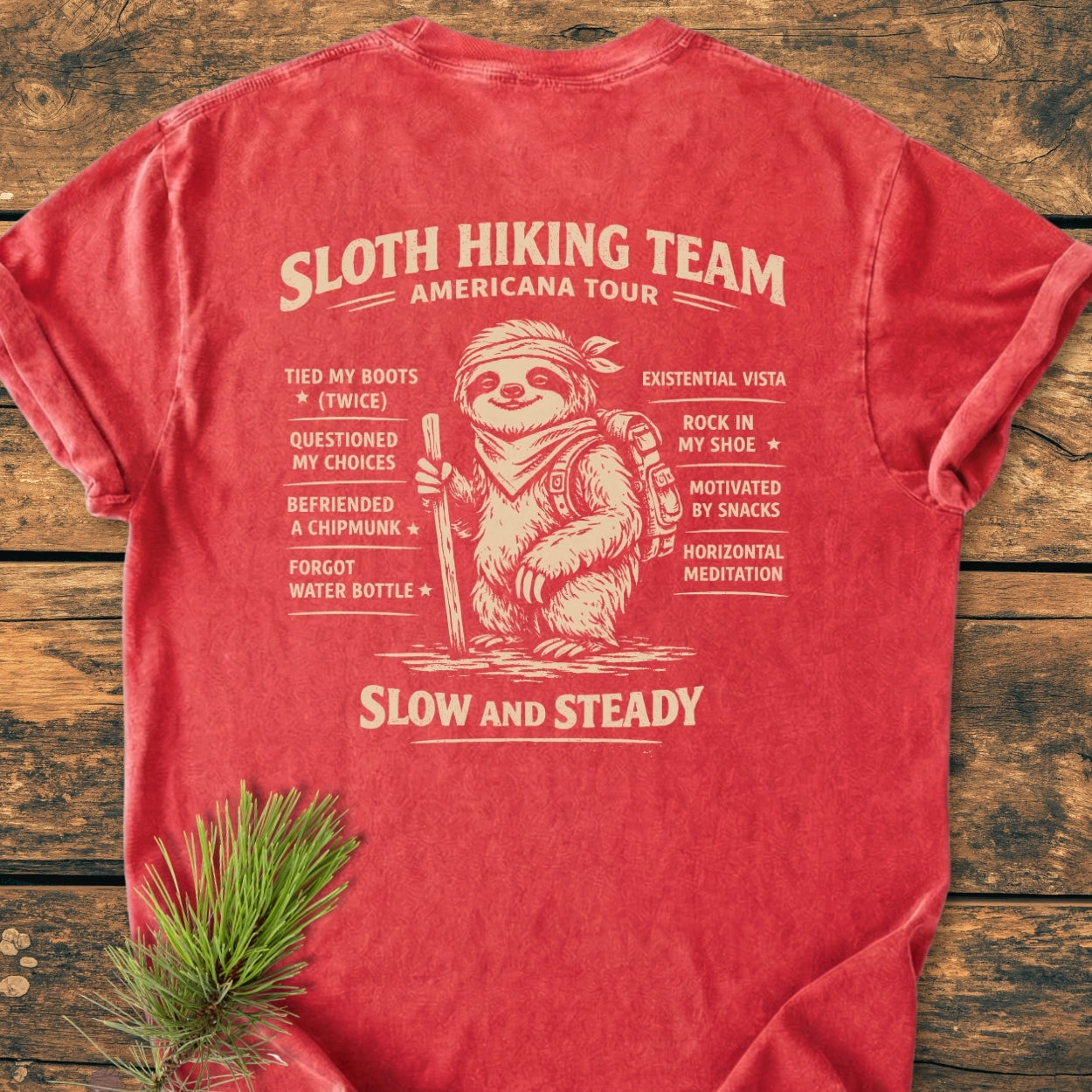 Sloth Hiking Team Tour BACK PRINT - Vintage Wash Tee featuring a smiling sloth with humorous hiking achievements on the back, laid flat, showcasing the relaxed fit and soft garment-dyed fabric.