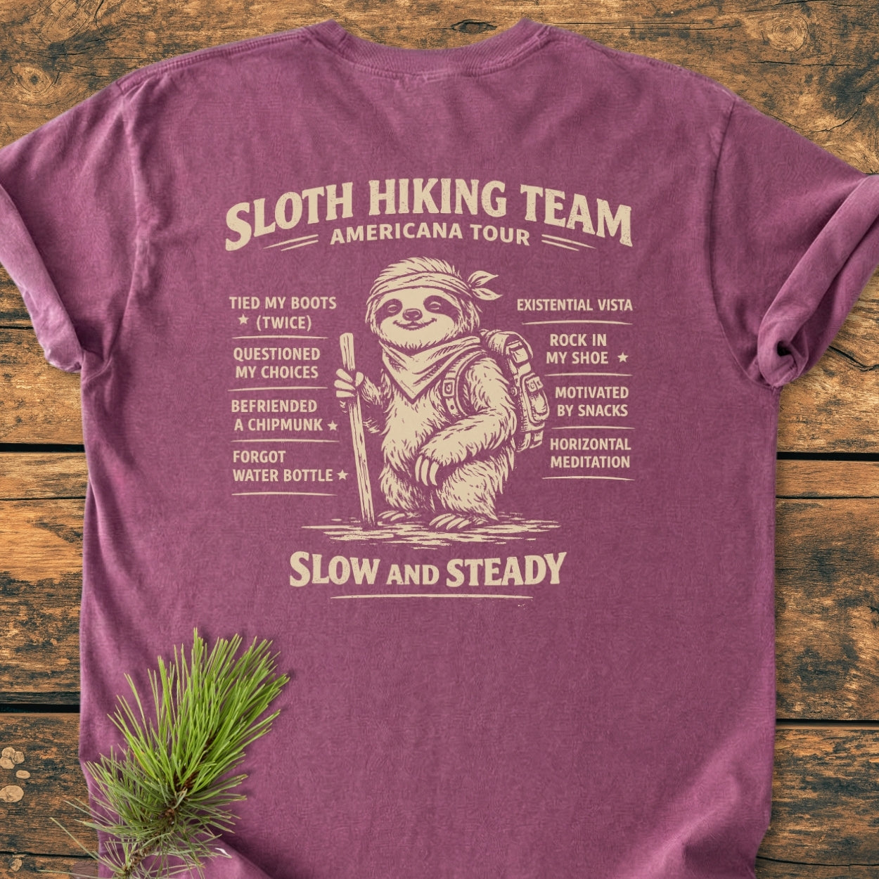 Sloth Hiking Team Tour BACK PRINT - Vintage Wash Tee featuring a sloth graphic with hiking milestones on a maroon T-shirt, laid flat, highlighting its relaxed fit and durable construction.