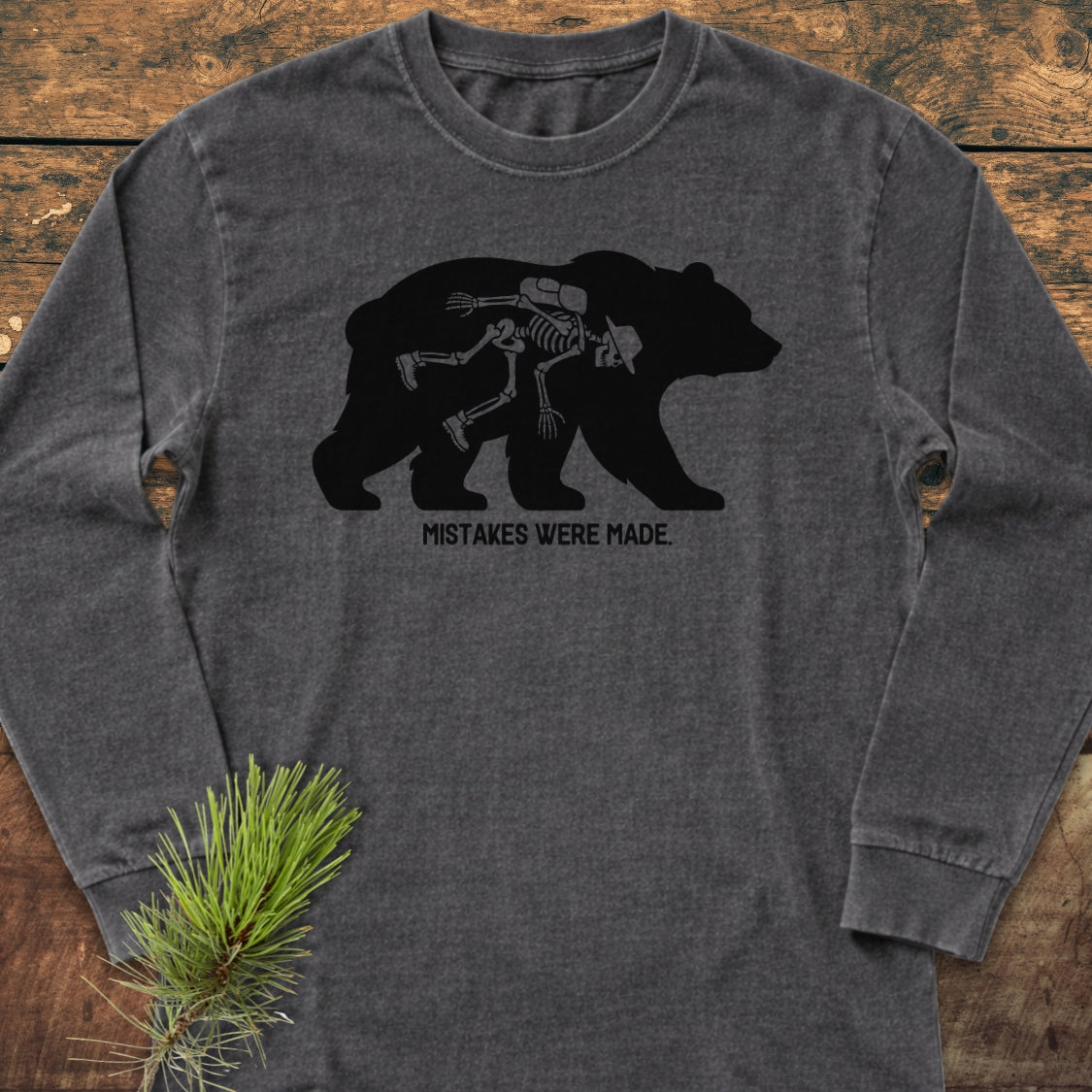 Mistakes Were Made Long-Sleeve Tee features a black bear silhouette with a hiker's skeleton inside, captioned “MISTAKES WERE MADE.” Made from soft, 100% ring-spun cotton for a relaxed, comfortable fit.
