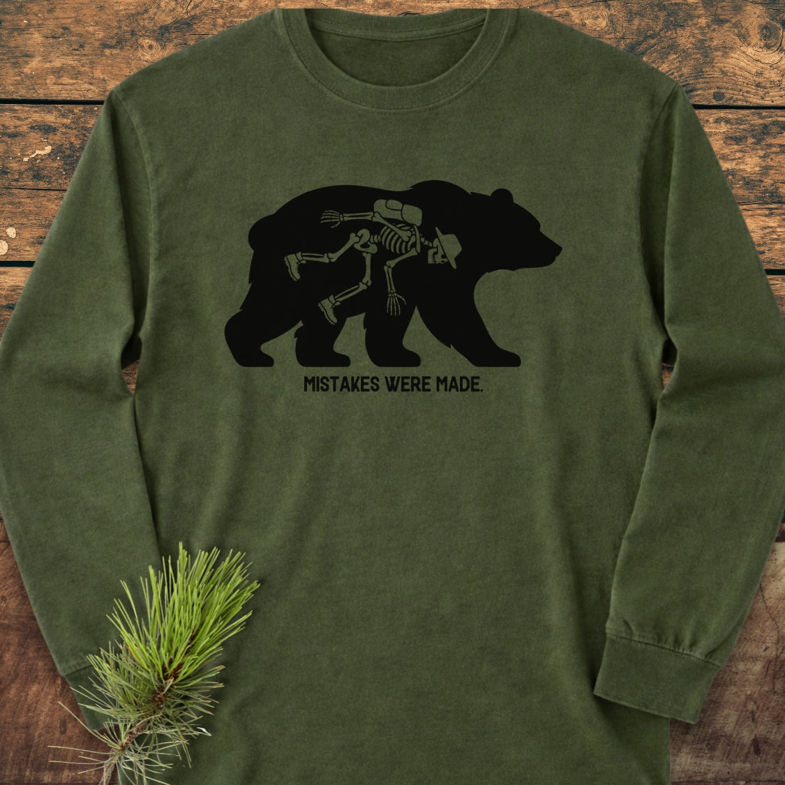 Mistakes Were Made Long-Sleeve Tee featuring a bear silhouette with a human skeleton inside, laid flat with a pine sprig. Made from 100% ring-spun cotton for a soft, relaxed fit.