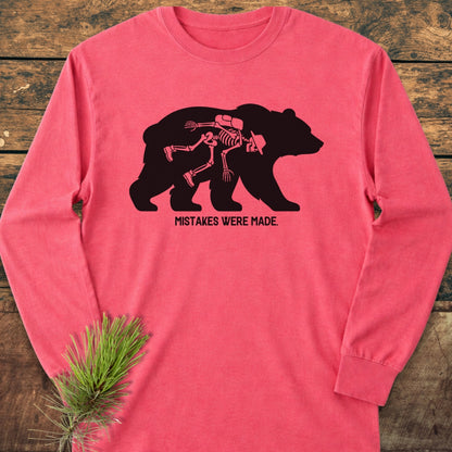 Mistakes Were Made Long-Sleeve Tee featuring a bold bear graphic with skeleton detail and humorous caption. Laid flat on a wooden surface, this 100% cotton tee offers a relaxed, stylish fit.