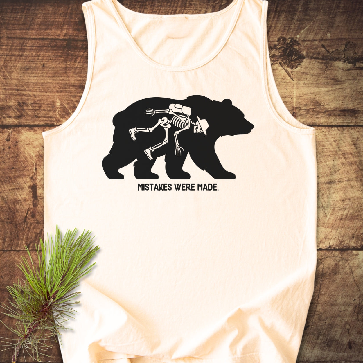 Off-white Mistakes Were Made Tank Top featuring a black bear silhouette with a skeleton hiker inside, accompanied by a pine sprig on a rustic wood background.