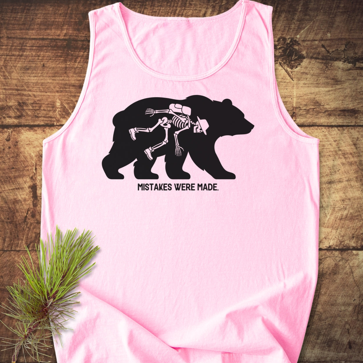 Mistakes Were Made Tank Top featuring a black bear silhouette with a hiker's skeleton inside, set on a pink background. The text MISTAKES WERE MADE. appears below the design, emphasizing style and sustainability.