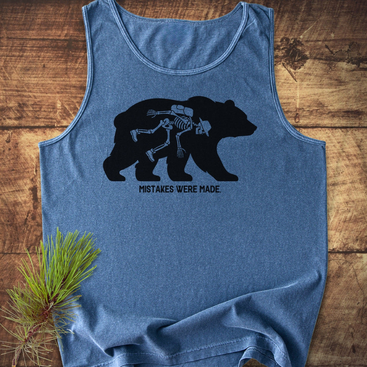Mistakes Were Made Tank Top features a heathered-blue sleeveless design with a bear silhouette revealing a human skeleton wearing hiking gear, emphasizing comfort and sustainability with its relaxed fit and ethical production.