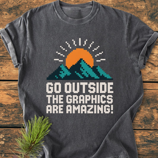 Go Outside Pixelart Mountain - Vintage Wash Tee featuring an 8-bit mountain and sun graphic on a dark gray background, laid on a wooden plank with a pine sprig nearby.