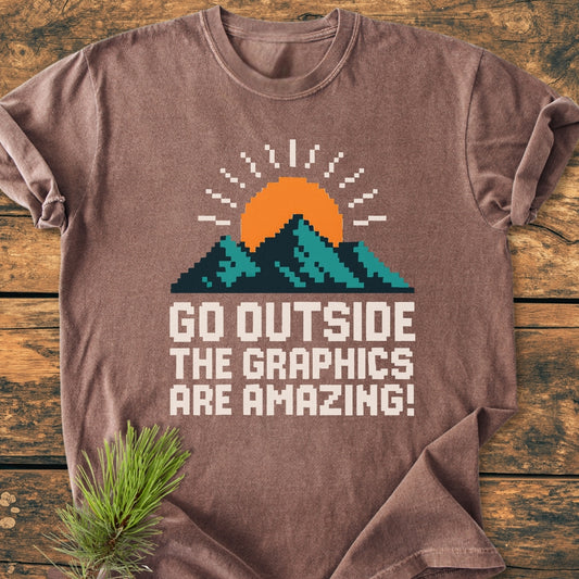 Go Outside Pixelart Mountain - Vintage Wash Tee laid on wood, features a retro pixel-art teal mountain graphic with an orange sun and white text, emphasizing comfort and durability with a relaxed fit.