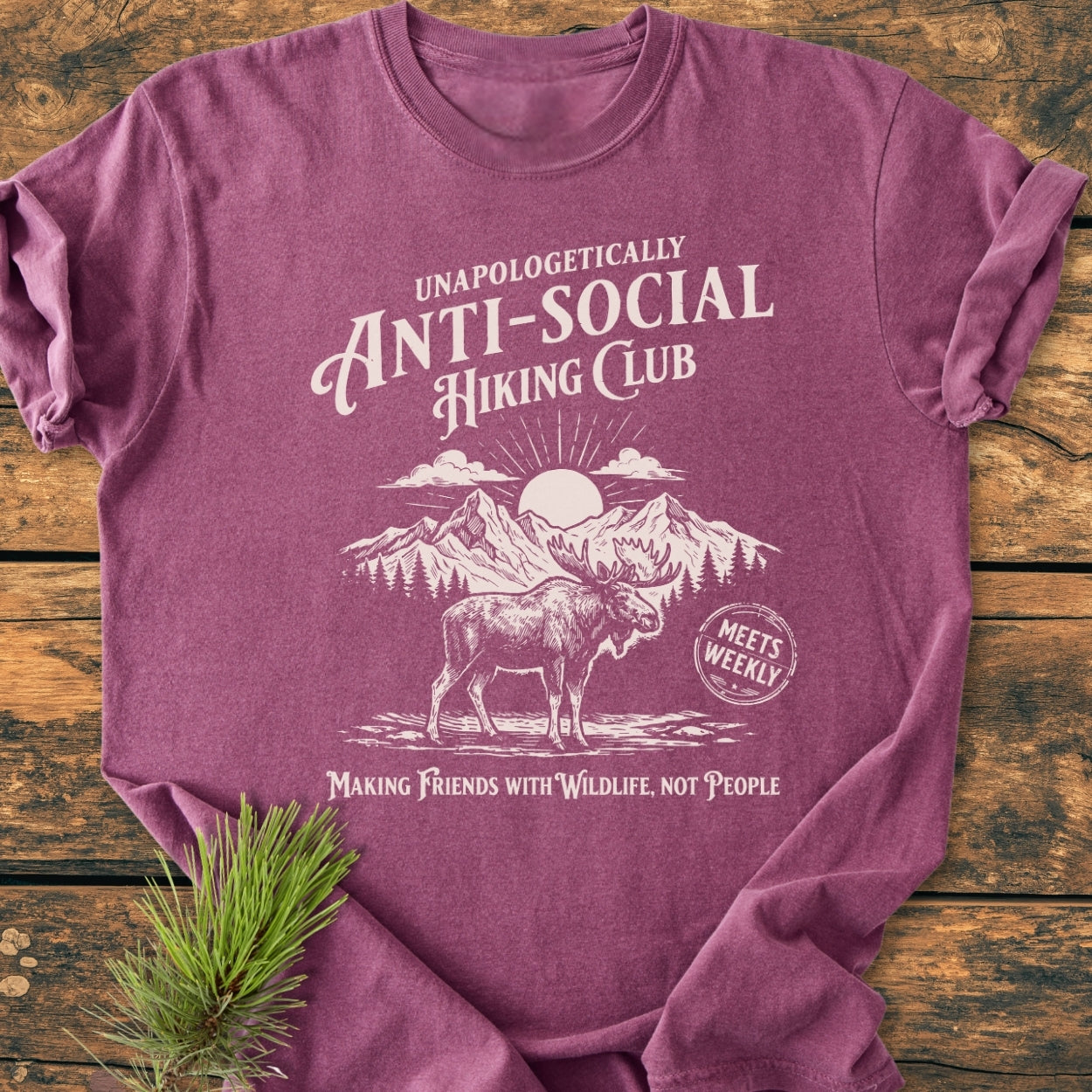 Anti-Social Hiking Club - Vintage Wash Tee featuring a hand-drawn moose graphic and slogan, laid on wood with pine sprig. Soft, durable, 100% ring-spun cotton, relaxed fit.