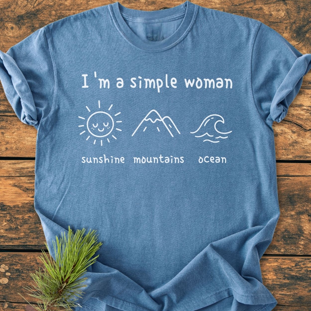 I'm A Simple Woman. Sunshine Mountains Ocean - Vintage Wash Tee; folded blue T-shirt features white minimalist sun, mountains, and ocean drawings, emphasizing comfort with soft, garment-dyed fabric and relaxed fit.