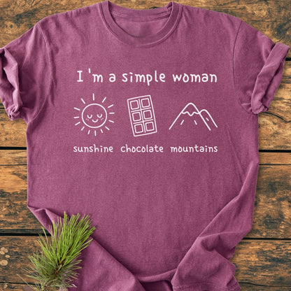 I'm A Simple Woman. Sunshine Chocolate Mountains - Vintage Wash Tee: Heather-plum T-shirt with white print of sun, chocolate bar, and mountain peak, displayed flat on a wooden surface.