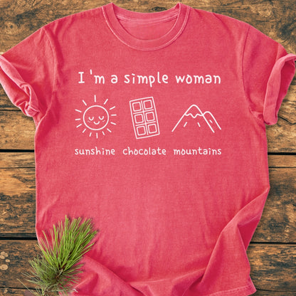 I'm A Simple Woman. Sunshine Chocolate Mountains - Vintage Wash Tee, featuring a relaxed fit with a white print of sun, chocolate, and mountain icons, laid on a wooden surface.