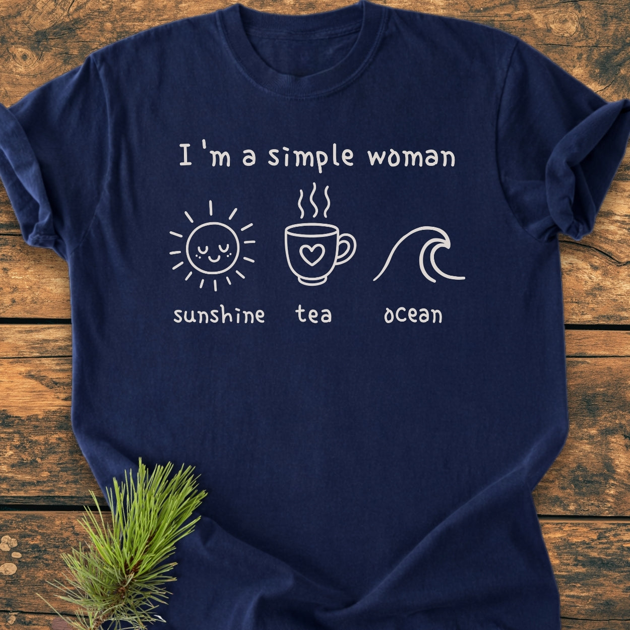 Navy-blue I'm A Simple Woman - Sunshine Tea Ocean - Vintage Wash Tee with white icons of a sun, teacup, and wave, laid on a wooden surface, showcasing its relaxed fit and casual style.