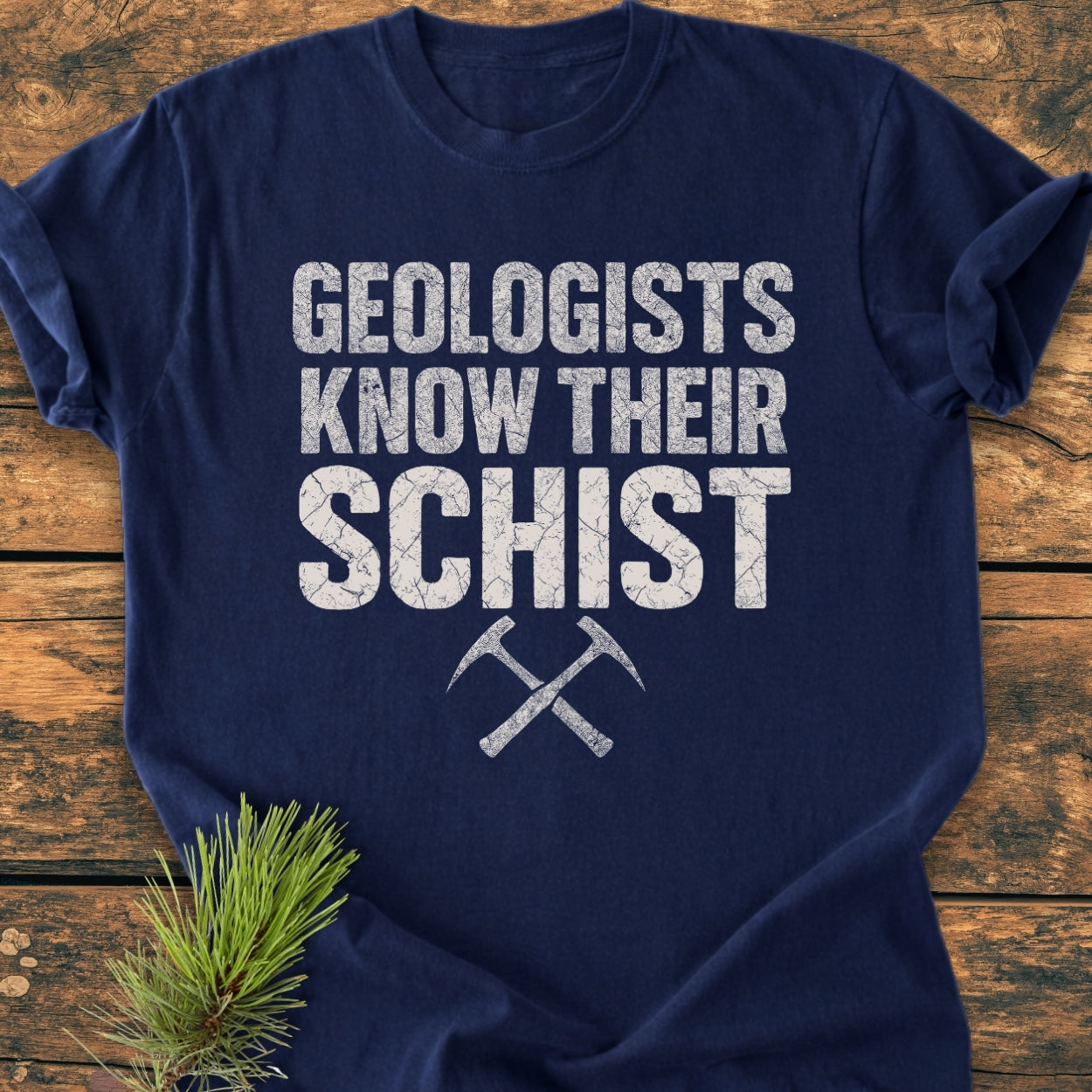 Navy-blue Geologists Know Their Schist - Vintage Wash Tee featuring a distressed white slogan and crossed rock-hammer graphic, laid flat on a wooden surface.