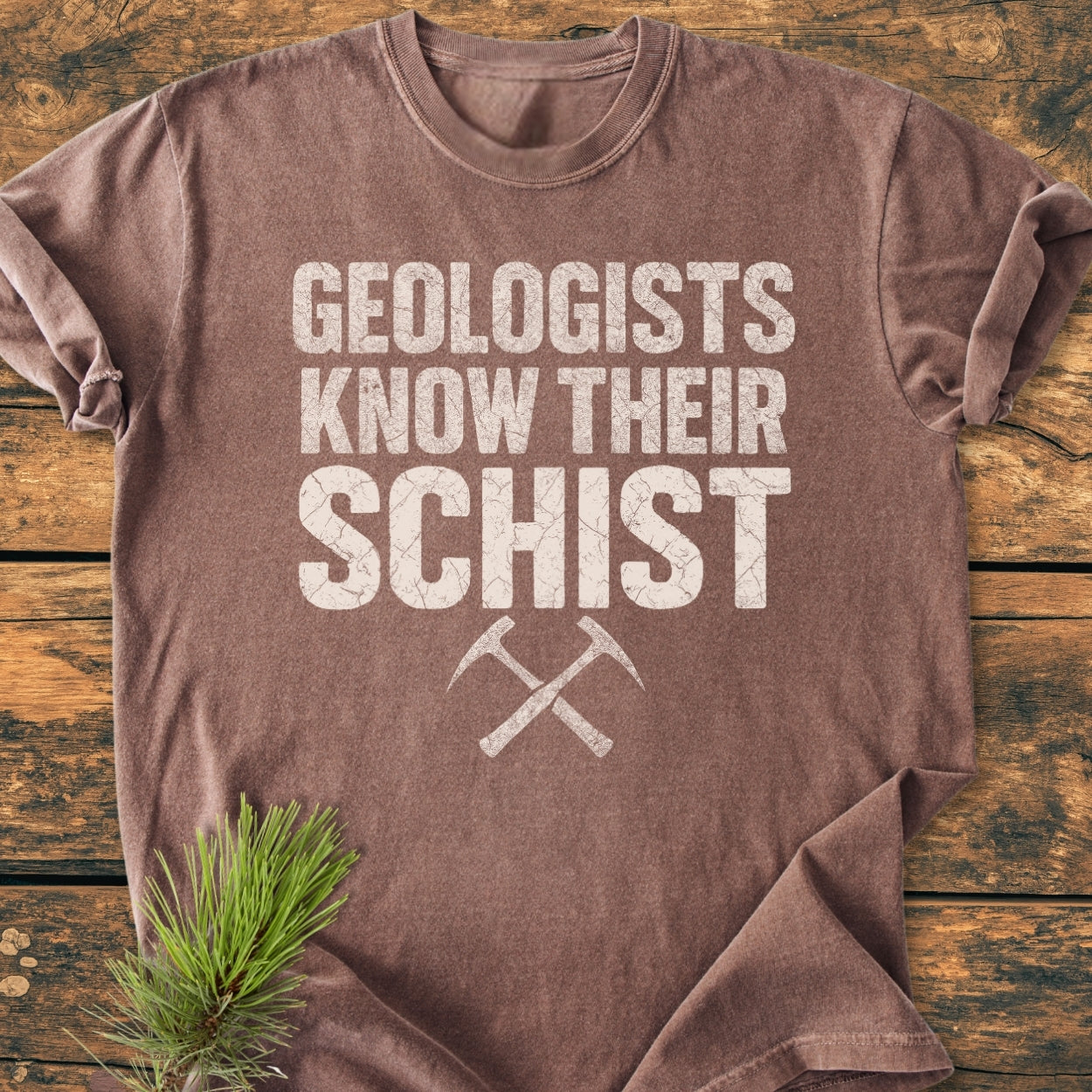 Geologists Know Their Schist - Vintage Wash Tee with bold white slogan and crossed pick-axes, laid on wood. Showcases relaxed fit and soft-washed, durable 100% ring-spun cotton construction.