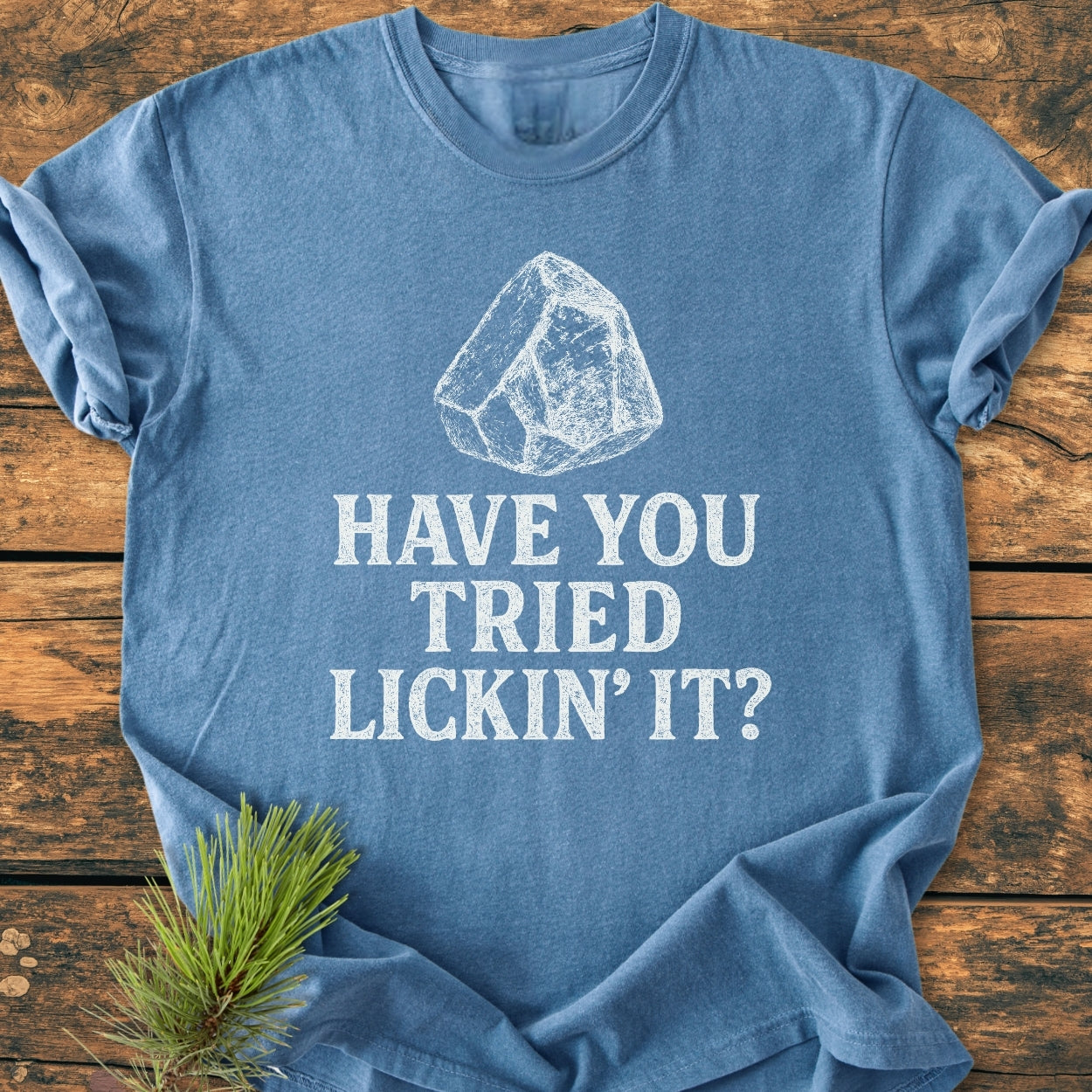 Heather-blue tee titled Have You Tried Lickin’ It? features a chalk-style rock graphic, laid on a wooden surface. Made from soft, durable, garment-dyed cotton with a relaxed fit.