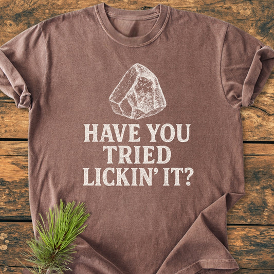 Brown Have You Tried Lickin' It? Rockhound - Vintage Wash Tee with white, chalk-style ice chunk sketch, laid on wood surface with pine sprig accent, showcasing its relaxed fit and soft-washed texture.