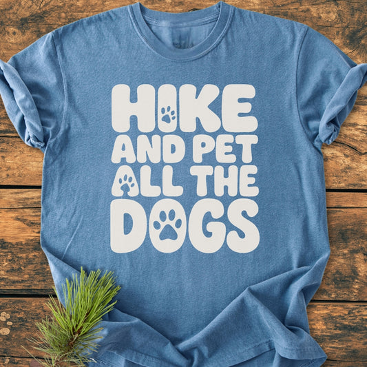 Heathered blue Hike And Pet All The Dogs - Vintage Wash Tee on rustic surface, featuring white bubble letters with paw prints. Includes pine twig accent. Soft, relaxed fit, durable, with tubular shape.