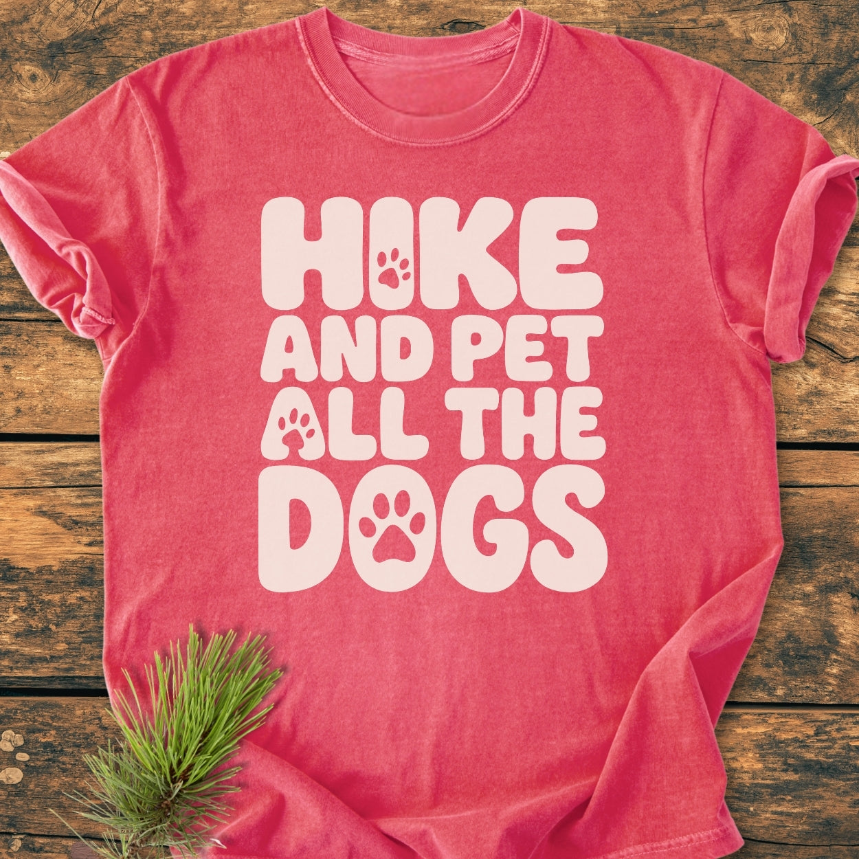 Hike And Pet All The Dogs - Vintage Wash Tee in heather-red features a playful slogan with paw-print icons on a rustic wood background, adorned with a pine sprig.