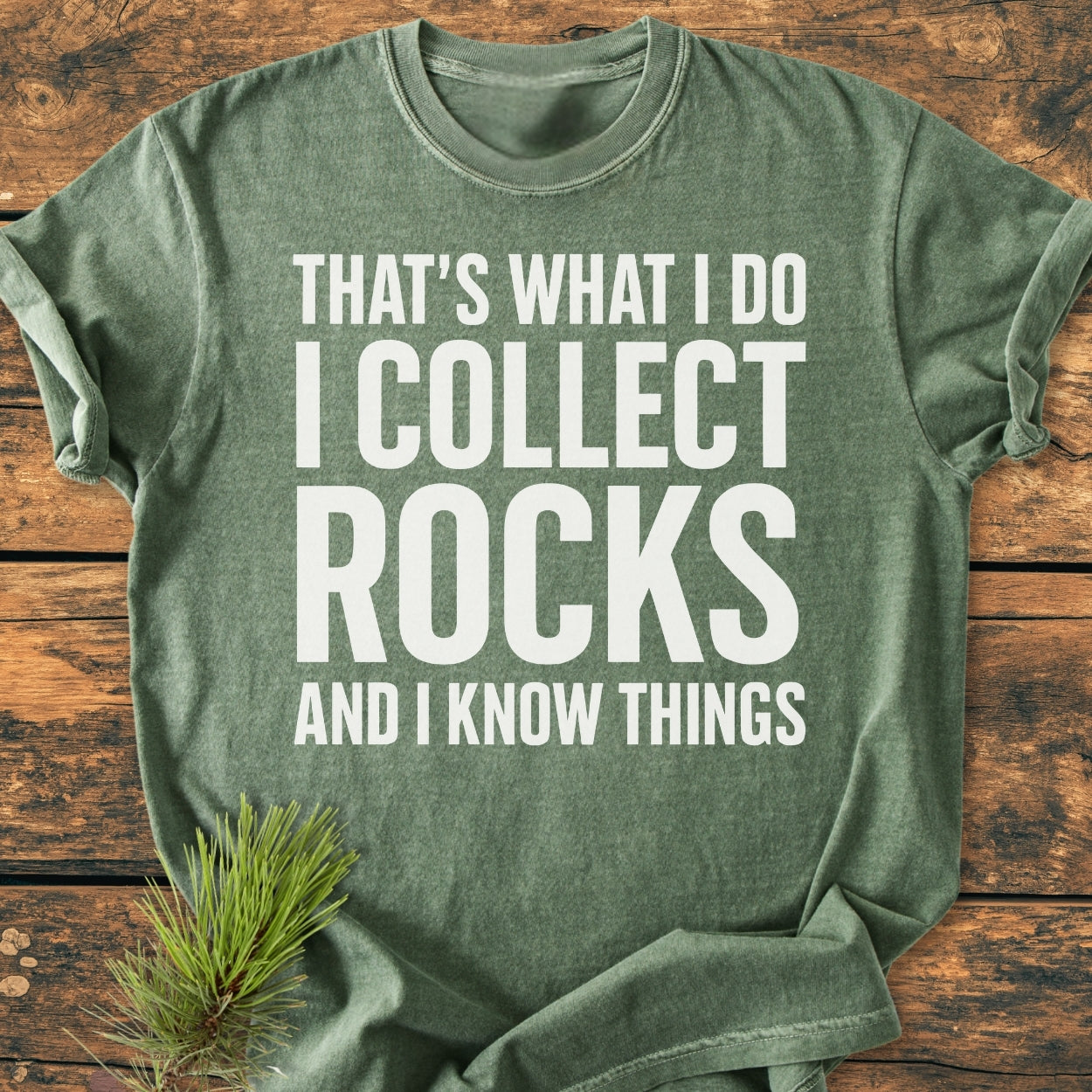 I Collect Rocks - Vintage Wash Tee, a green heathered T-shirt with a white block-lettered phrase, laid flat on wood, featuring a pine sprig. Comfortable, durable, and relaxed fit for everyday wear.