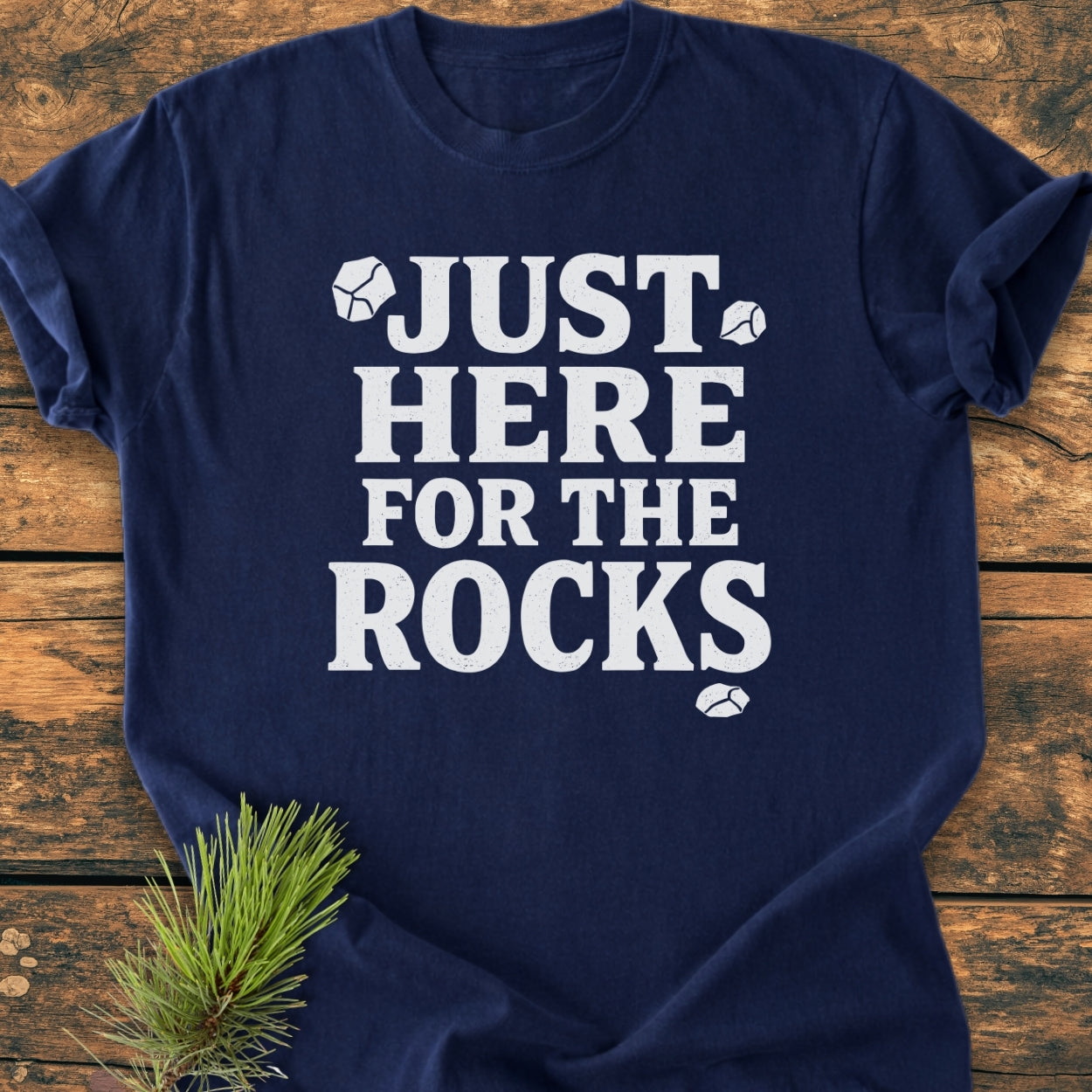 Just Here For The Rocks - Vintage Wash Tee features bold white text with rock illustrations on a navy-blue T-shirt, laid flat on wood, showcasing its relaxed fit and soft fabric.