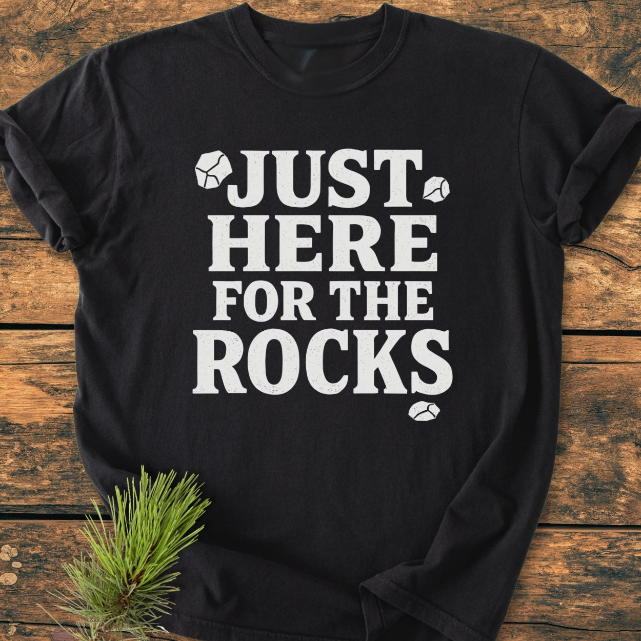 Just Here For The Rocks - Vintage Wash Tee displayed on wood, features bold white text and rock icons. Made from soft-washed, 100% ring-spun cotton, offering comfort and durability.