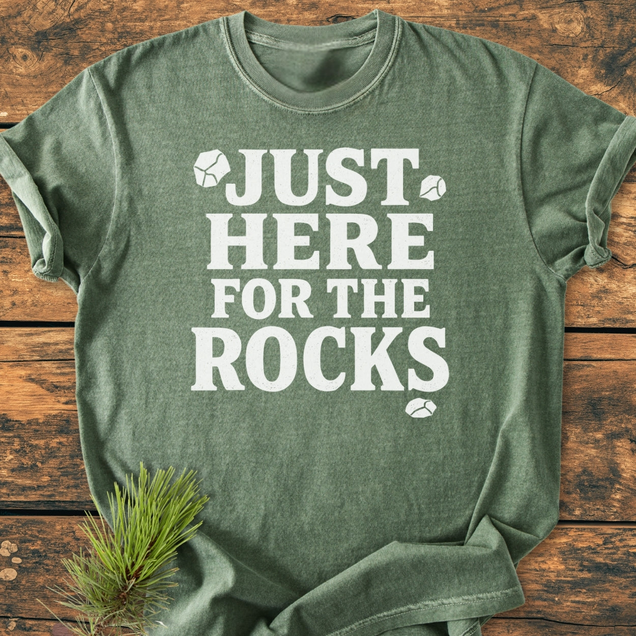 Green Just Here For The Rocks - Vintage Wash Tee with off-white text and rock icons, laid flat on wood. Features soft, relaxed fit, double-needle stitching, and durable garment-dyed cotton fabric.