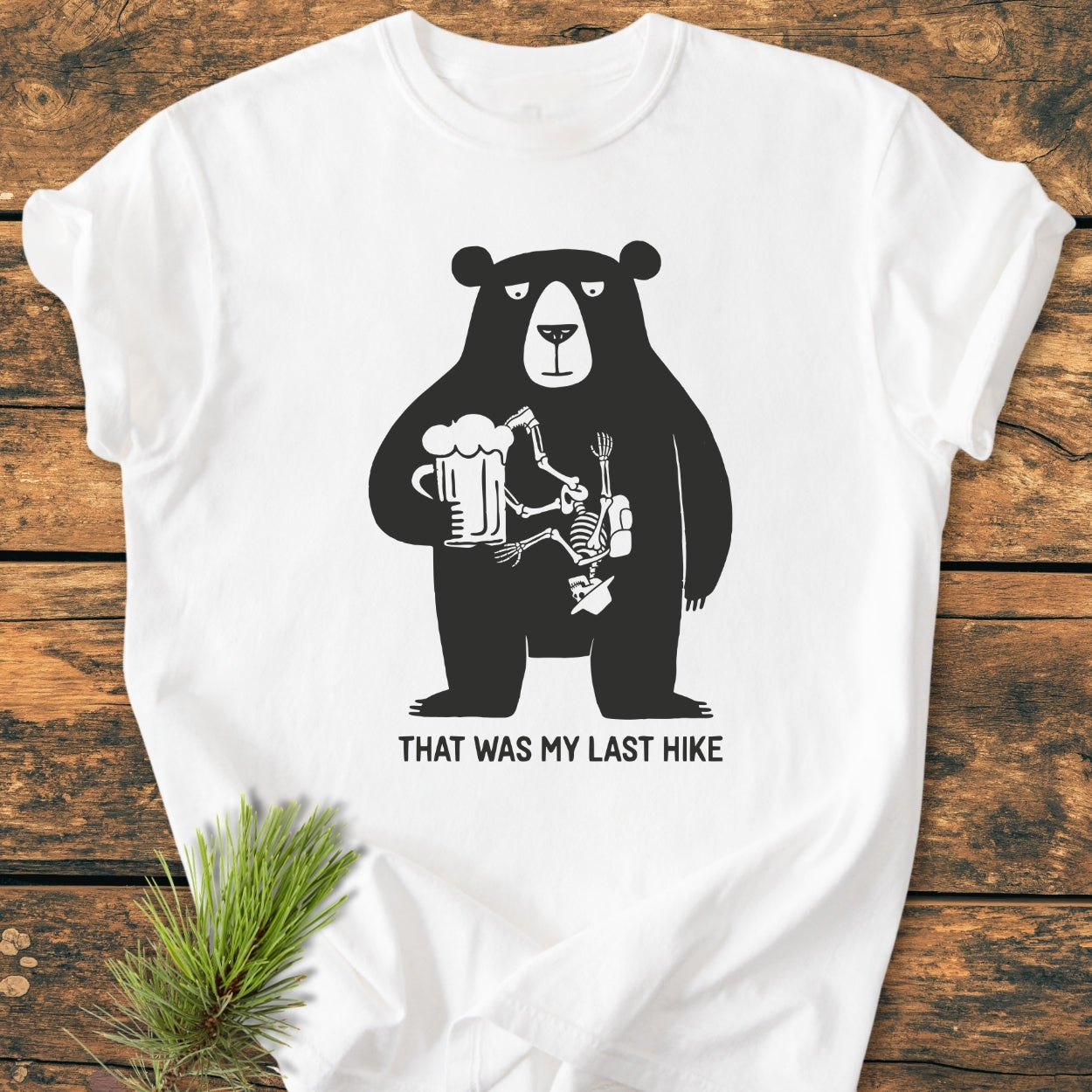 That Was My Last Hike - Vintage Wash Tee featuring a cartoon bear with a beer and a hiker's skeleton inside, laid flat. The T-shirt is made from soft, durable, garment-dyed cotton.