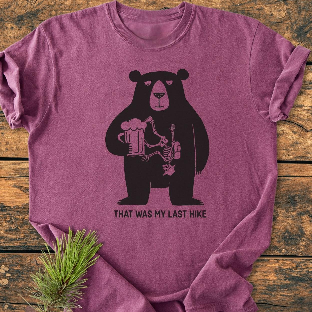 That Was My Last Hike - Vintage Wash Tee features a bear silhouette with a skeleton inside, holding a beer mug, captioned humorously. Laid flat, highlighting its soft, relaxed fit and durable construction.