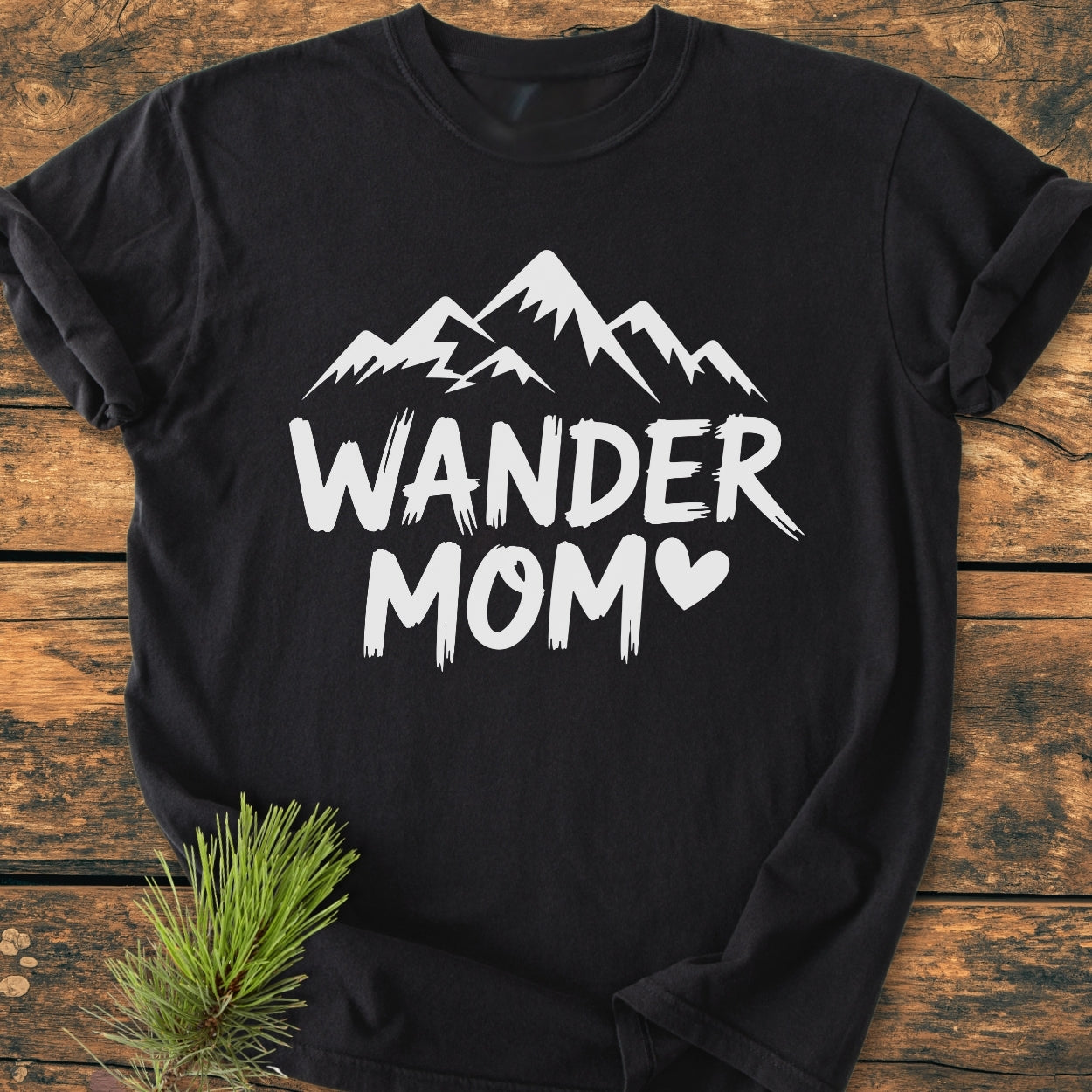 Wander Mom - Vintage Wash Tee featuring a stylized mountain and heart design on the front; displayed on wood, highlighting the tee’s relaxed fit and soft, garment-dyed cotton texture.