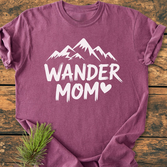 Wander Mom - Vintage Wash Tee in plum, featuring a mountain silhouette and heart-shaped O. Laid on wood with pine sprig, highlighting its soft, durable design and relaxed fit.