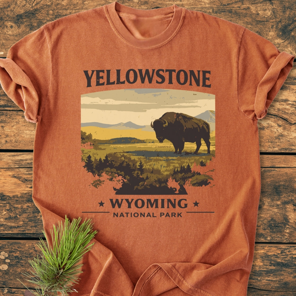 Yellowstone - Vintage Wash Tee features a bison scene on rust-orange fabric, laid flat on wood. Garment-dyed for coziness, this tee is crafted from pre-shrunk, ring-spun cotton.