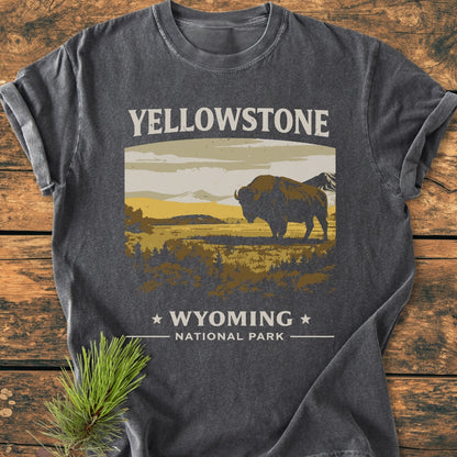 Yellowstone - Vintage Wash Tee featuring a bison graphic in a Yellowstone landscape. Laid on wood with a pine sprig, highlighting the durable, relaxed-fit, garment-dyed Comfort Colors 1717 T-shirt.