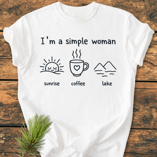 I'm A Simple Woman - Sunrise Coffee Lake - Vintage Wash Tee features a casual white T-shirt with hand-drawn icons: sunrise, coffee, and a lake, laid flat on a wooden surface.