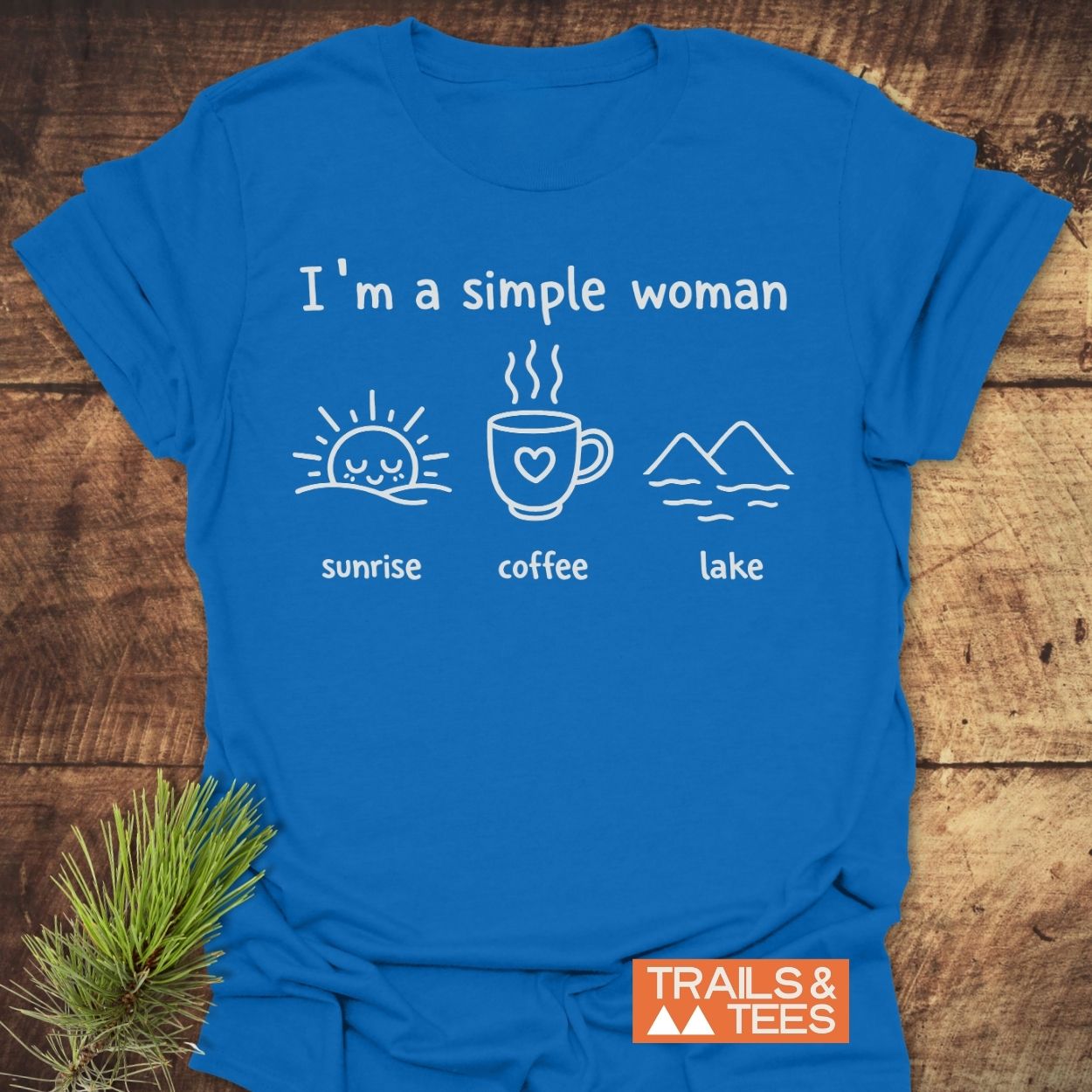 I'm A Simple Woman - Sunrise Coffee Lake T-Shirt displayed on wood, featuring white prints: sunrise, coffee, lake. Orange TRAILS & TEES logo at corner.
