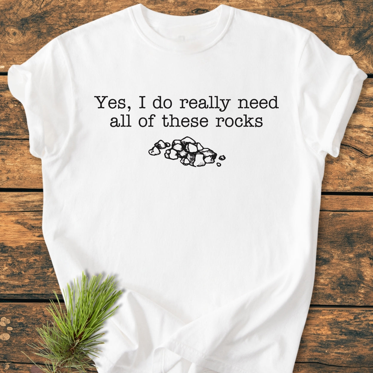 All These Rocks - Vintage Wash Tee features a typewriter-style quote and rock drawing on a laid-out white T-shirt, adorned with a pine sprig, crafted from 100% ring-spun cotton for comfort.