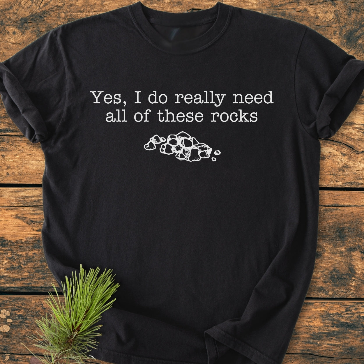 All These Rocks - Vintage Wash Tee: Black T-shirt with white text Yes, I do really need all of these rocks and rock illustration, featuring soft-washed fabric and relaxed fit, displayed on a wooden surface.