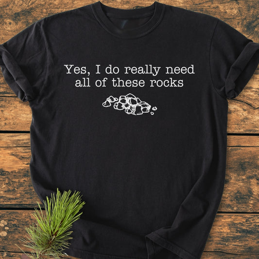 All These Rocks - Vintage Wash Tee: Black T-shirt with white text Yes, I do really need all of these rocks and rock illustration, featuring soft-washed fabric and relaxed fit, displayed on a wooden surface.