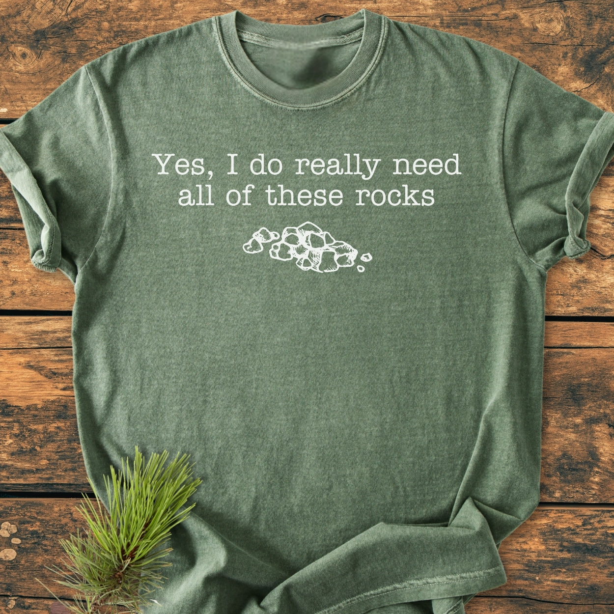 All These Rocks - Vintage Wash Tee in heather-green with white text and stone drawing, laid on rustic wood. Features soft, garment-dyed fabric, relaxed fit, and durable double-needle stitching.