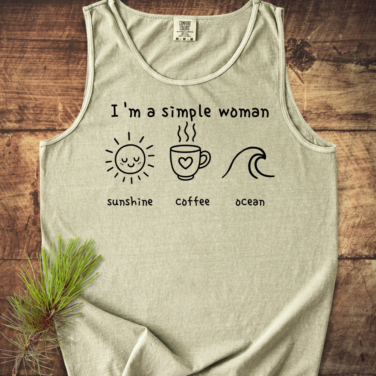 I'm A Simple Woman - Sunshine Coffee Ocean Tank Top: Light-grey tank top featuring black line-drawings of a sun, coffee mug, and wave, each with captions, laid on a wooden surface.
