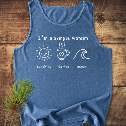 I'm A Simple Woman - Sunshine Coffee Ocean Tank Top: A blue sleeveless garment featuring white lettering and icons of a sun, coffee cup, and ocean wave, laid on a wooden surface.