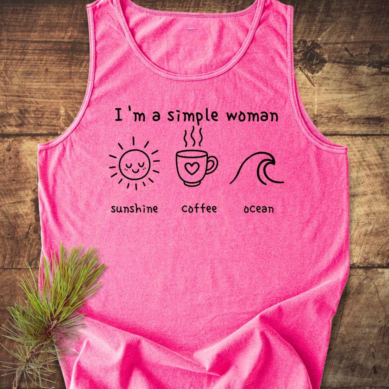 I'm A Simple Woman - Sunshine Coffee Ocean Tank Top displayed on wood with a pine sprig. Features bright pink color, black print with sun, coffee mug, wave, highlighting comfort and sustainability.
