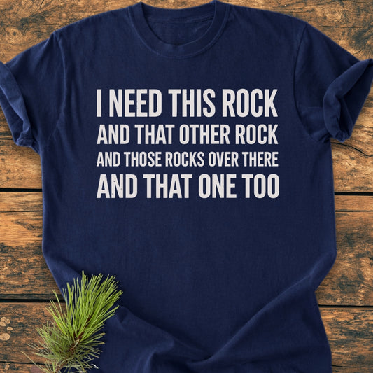 I Need This Rock - Vintage Wash Tee featuring white block text on a navy blue T-shirt, displayed on rustic wood with a pine sprig accent, emphasizing comfort and relaxed fit.