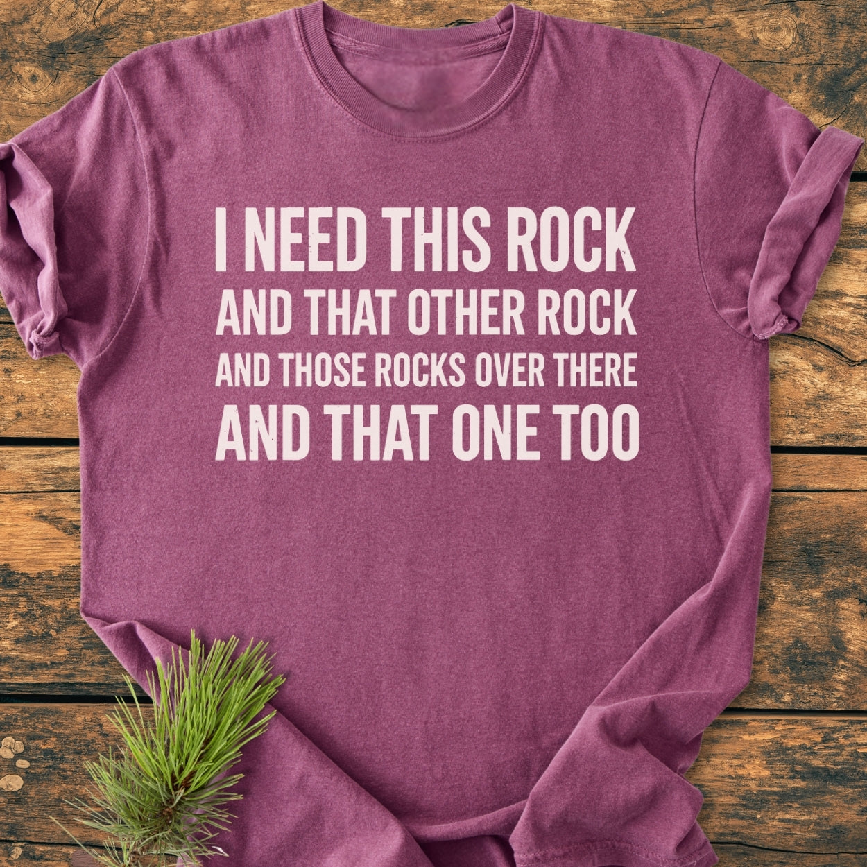 Heather-purple I Need This Rock - Vintage Wash Tee with bold white slogan on the front, displayed on wooden surface with pine sprig. Crew-neck, relaxed fit, soft-washed garment-dyed cotton.